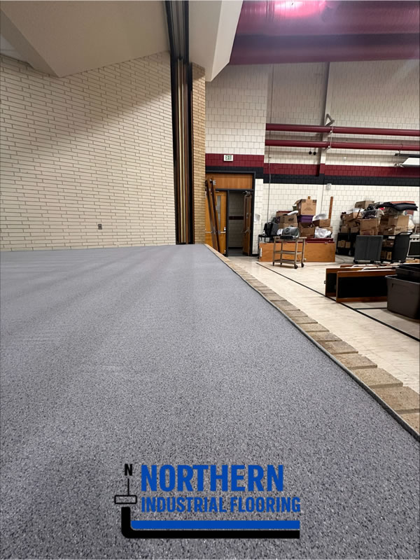 Indoor industrial space with a long stretch of fresh gray epoxy flooring; logo for Northern Industrial Flooring is in the foreground.